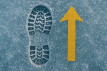 Boot prints and an arrow drawn in the snow next to a drilled lane