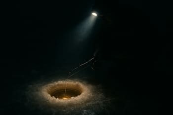 Lantern-lit line of holes with headlamp beams cutting through falling snow